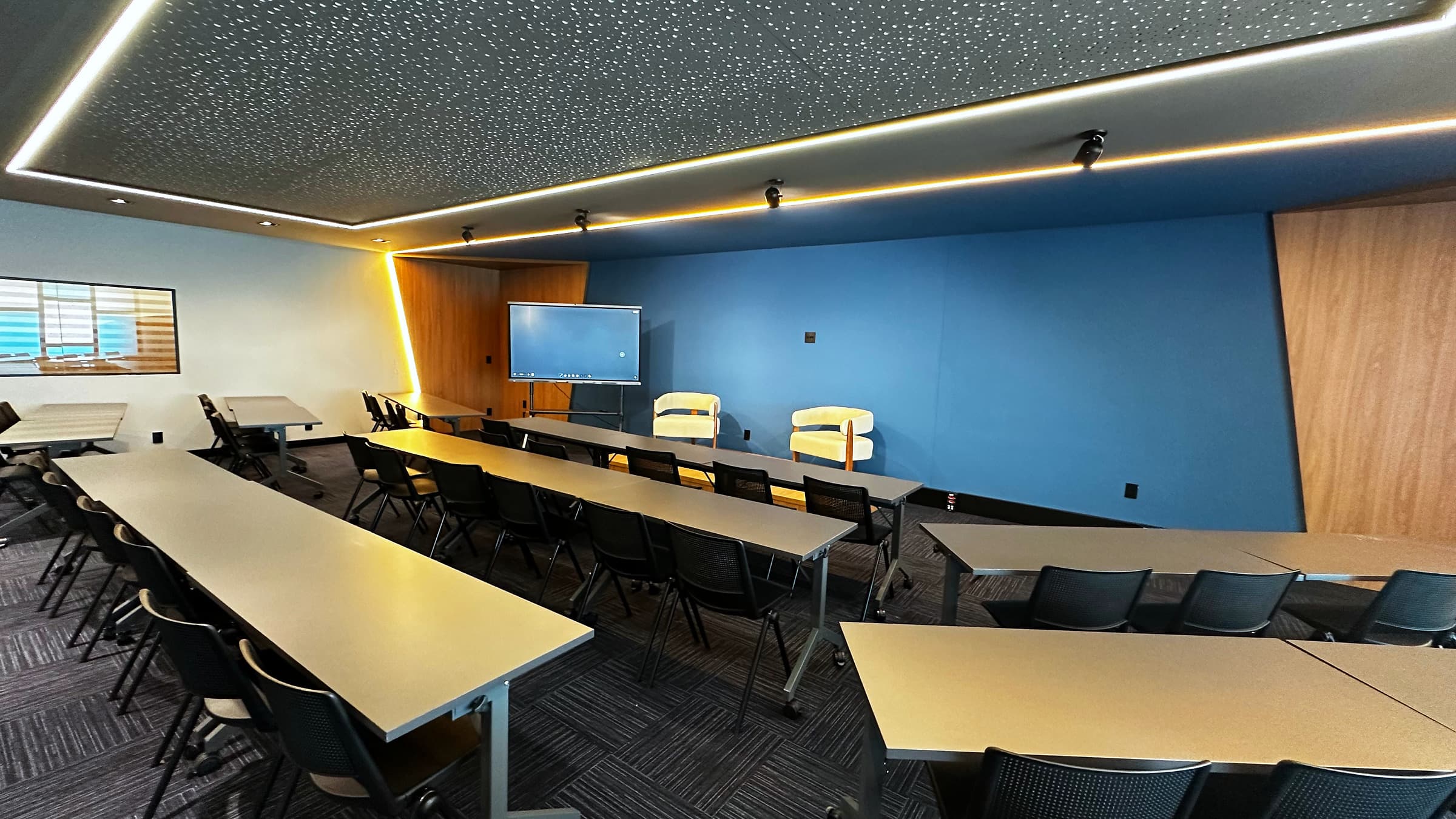 Sala de treinamento da escola em Campinas: bancadas, cadeiras e telas nas paredes.